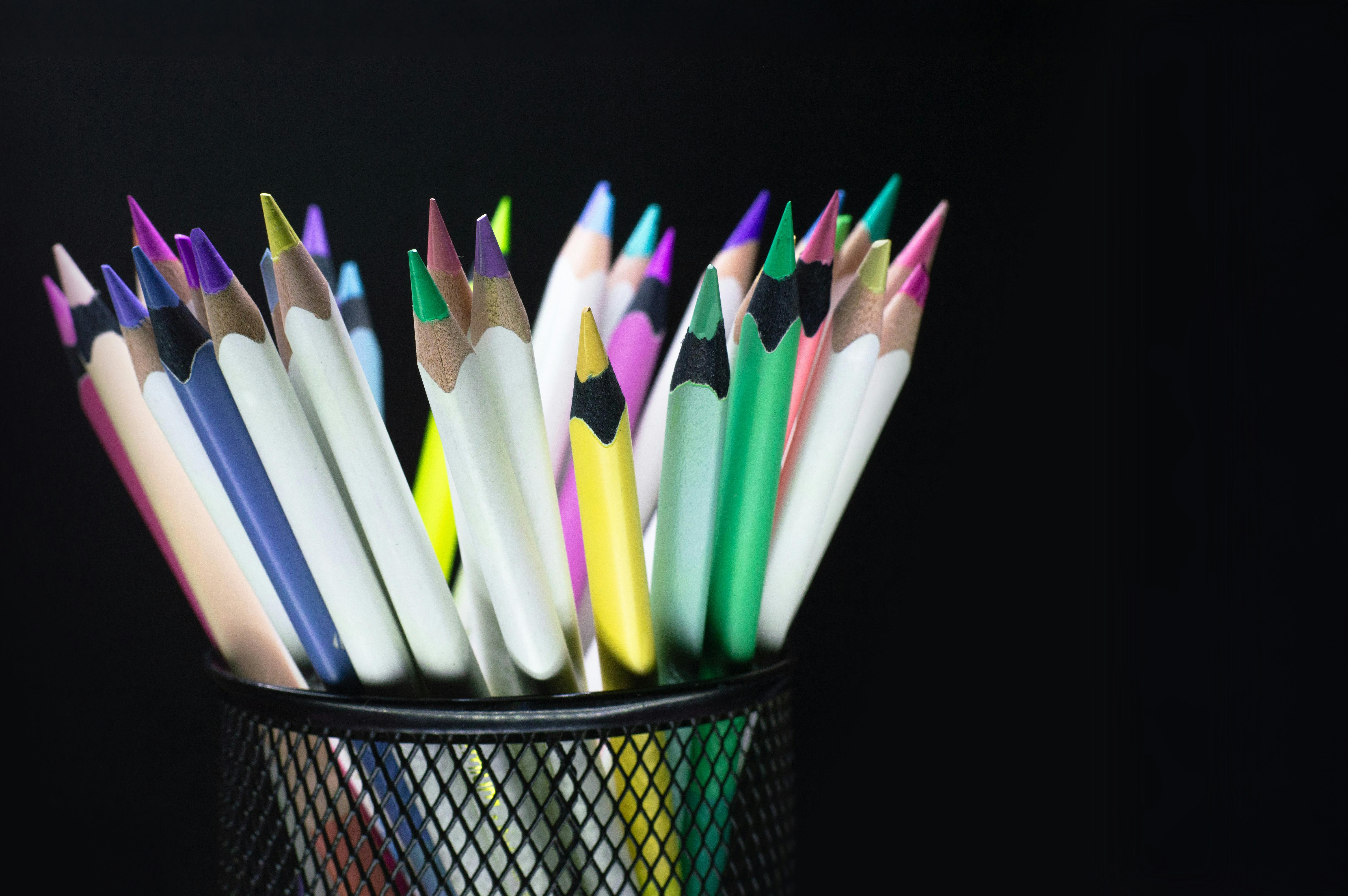 Assorted colorful pencils organized in a black mesh pencil holder against a dark backdrop.