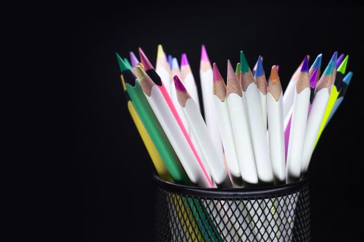 A vibrant collection of colored pencils in a mesh holder against a dark background.