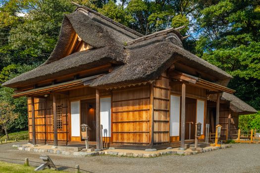 Charming wooden minka with thatched roof nestled in a tranquil Japanese garden.