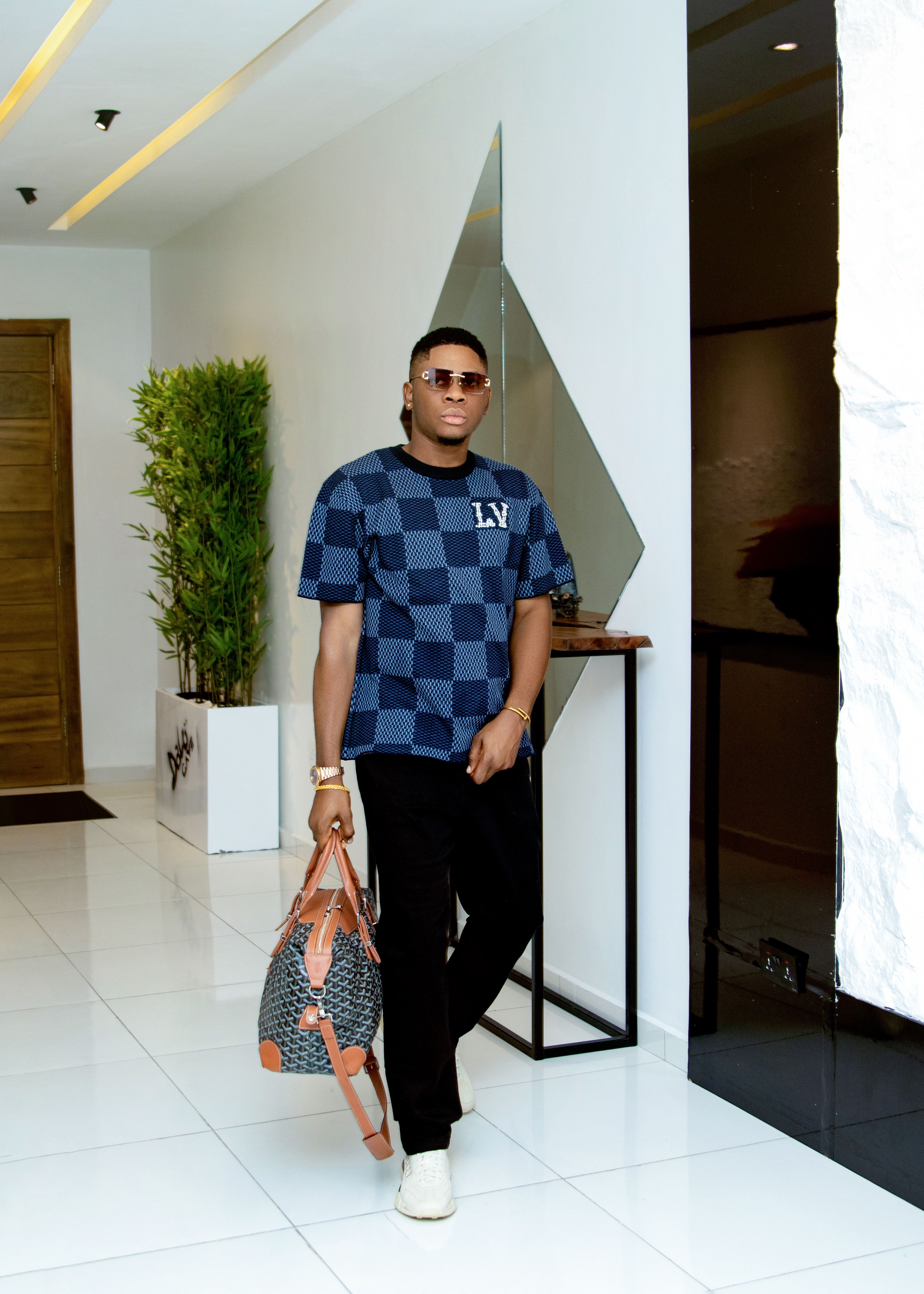 Stylish man in designer outfit holding luxury bag indoors.