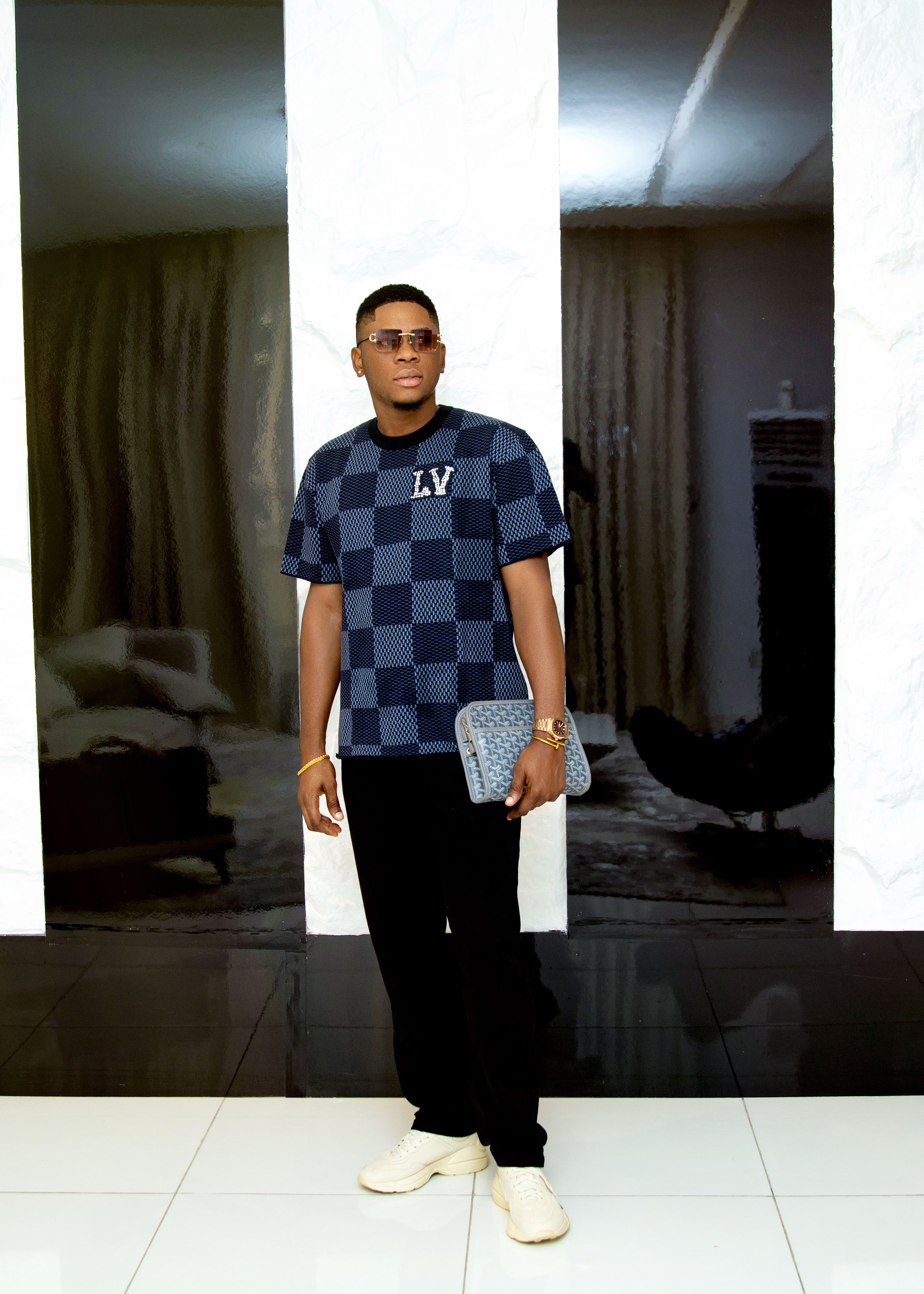 Fashionable adult male in designer attire holding luxury bag indoors.