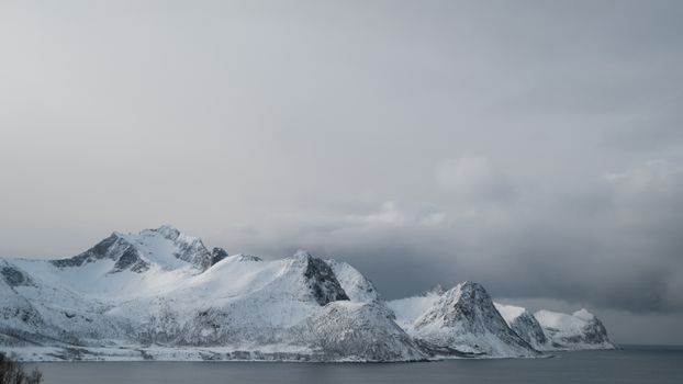 Captivating view of snow-covered mountains by the sea under a cloudy sky.