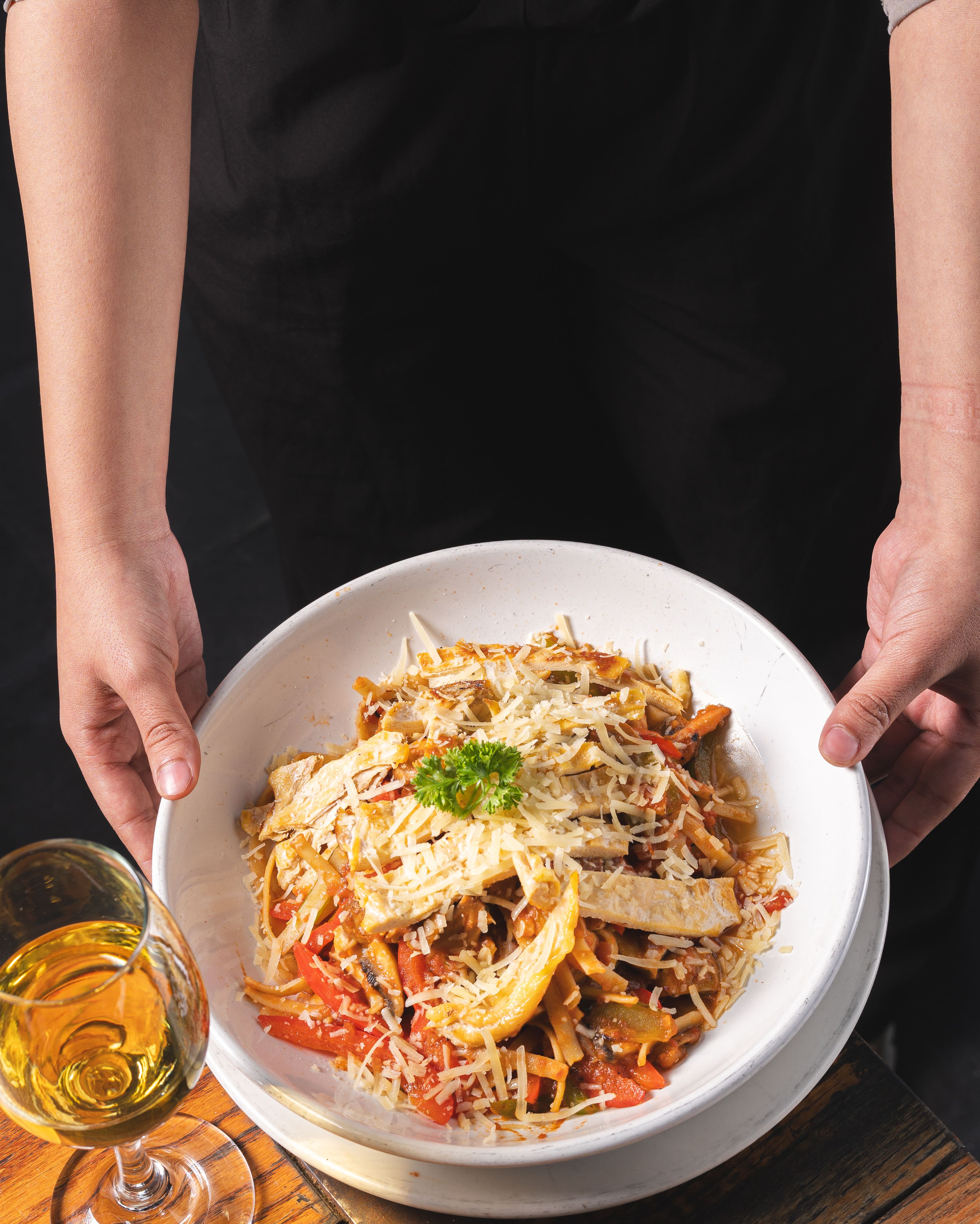 A plate of flavorful pasta topped with parmesan and parsley, served with white wine.