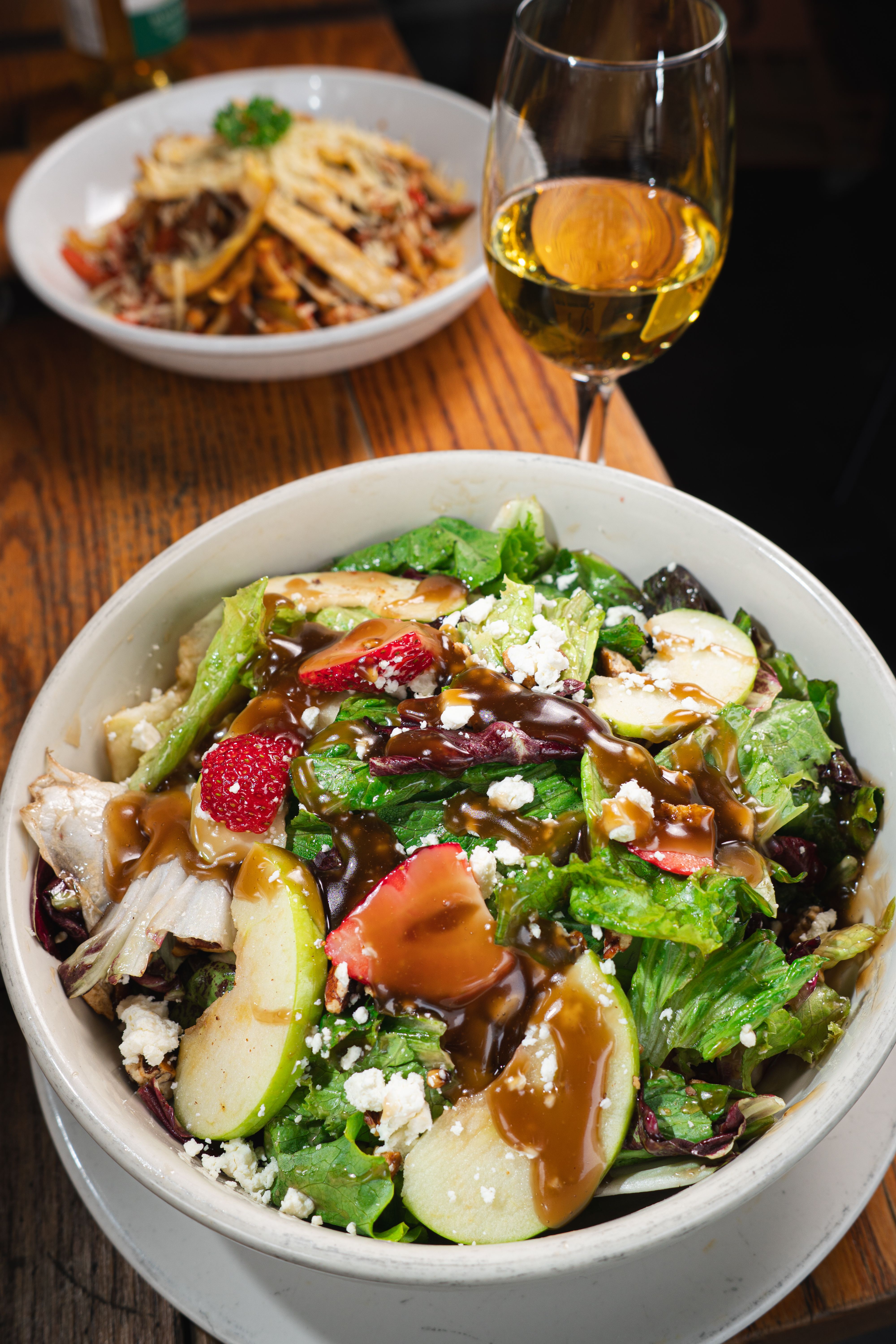 Close-up view of a fresh salad and Italian pasta accompanied by a glass of white wine on a rustic table.