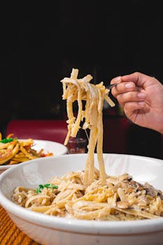 Close-up of creamy fettuccine alfredo being lifted by hand, emphasizing gourmet Italian cuisine.