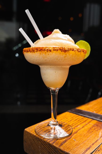 Two salt-rimmed margarita glasses filled with bright orange frozen mango margarita, garnished with lime wheels and a mango slice.