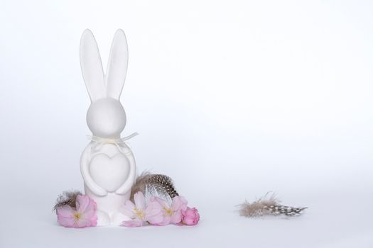 White ceramic bunny with heart surrounded by cherry blossoms and feathers on a white background.