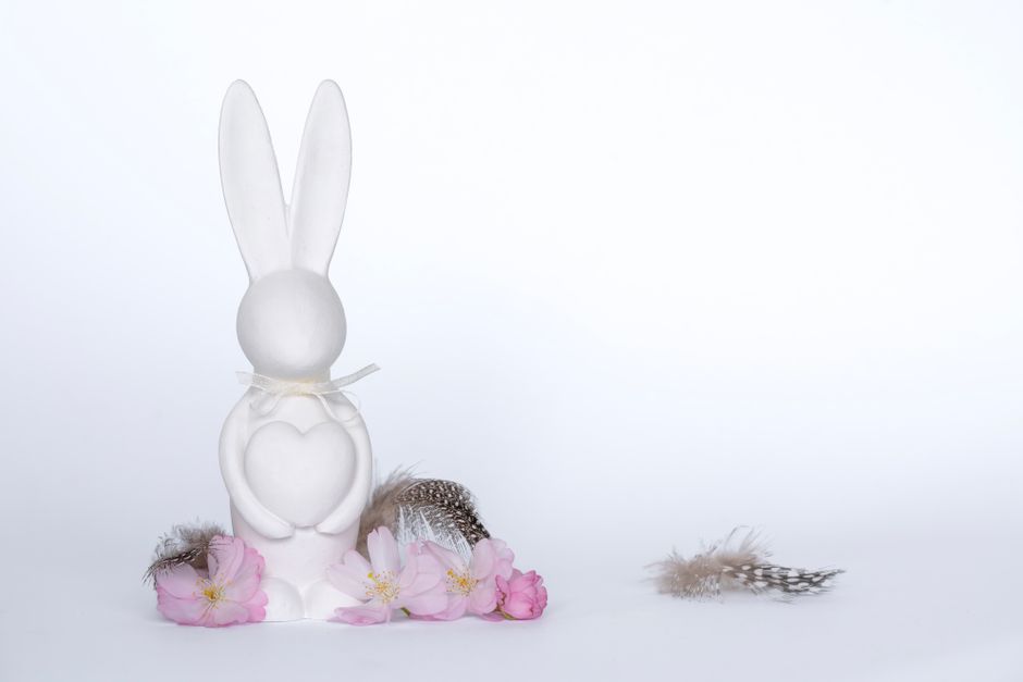 White ceramic bunny with heart surrounded by cherry blossoms and feathers on a white background.