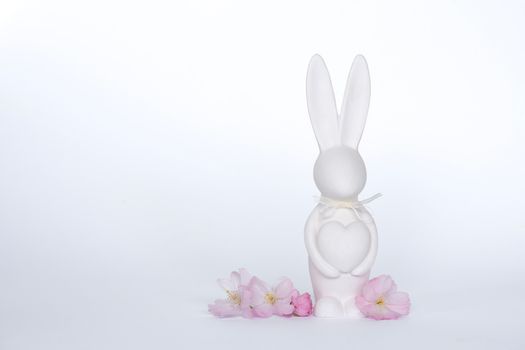 Charming white rabbit ornament with heart symbol, surrounded by sakura blossoms on a white background.