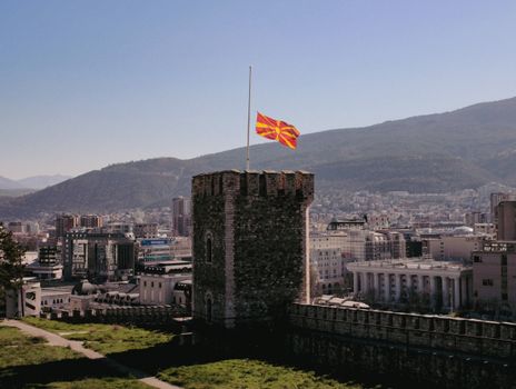 Historic stone tower with the Macedonian flag overlooks Skopje skyline.