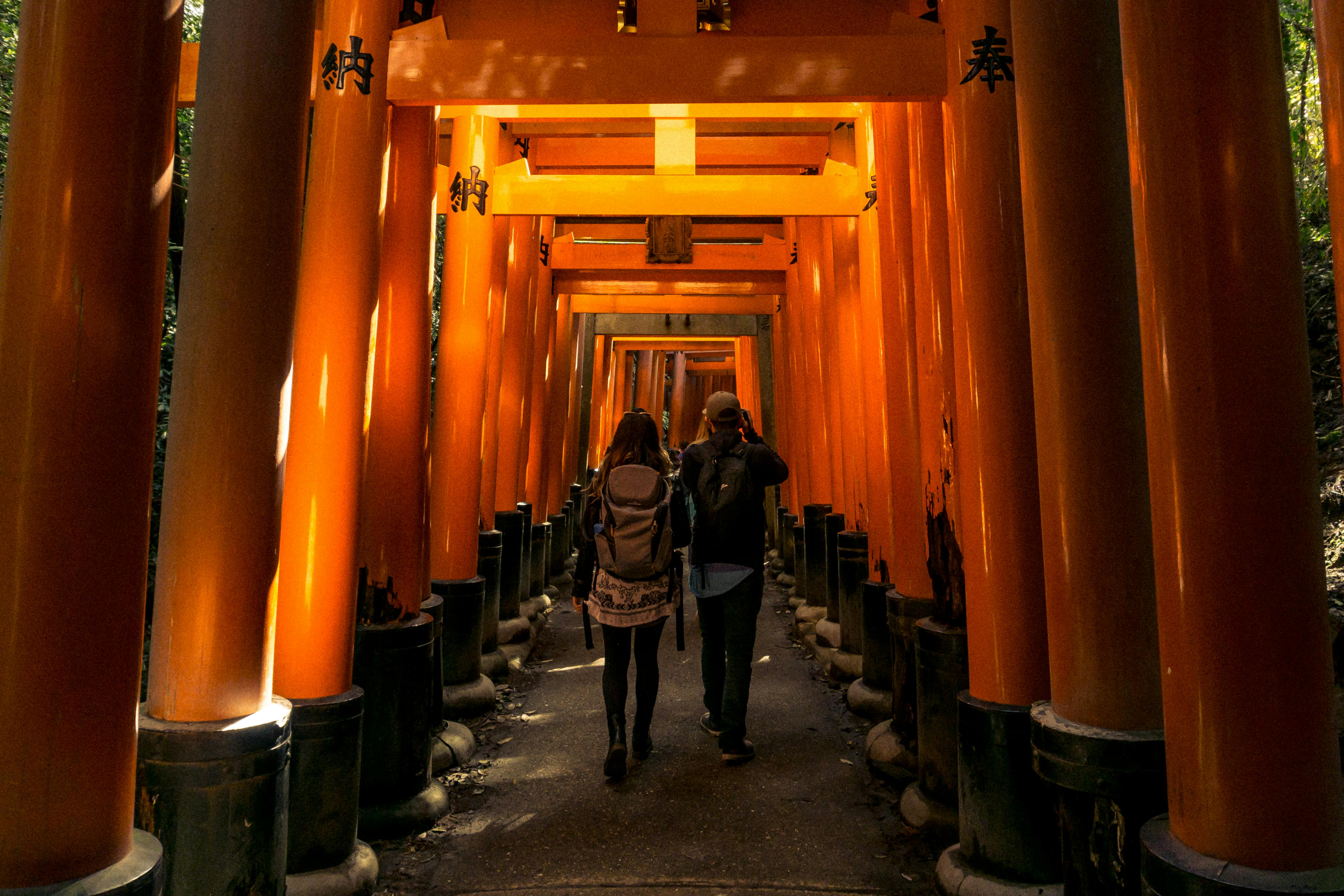 A couple walks through the iconic orange torii gates at Fushimi Inari Shrine in Kyoto, Japan.
