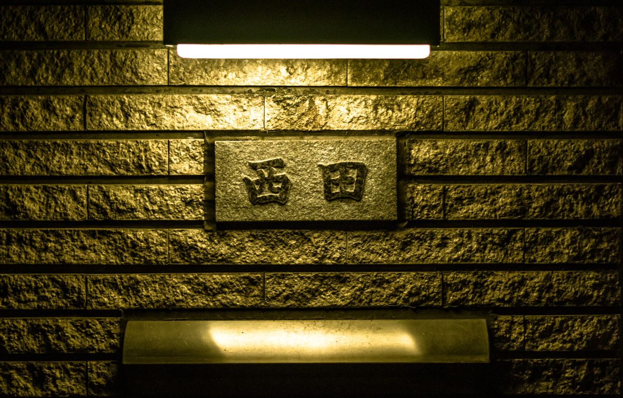 a plaque with japanese characters on a lit brick wall creating a moody