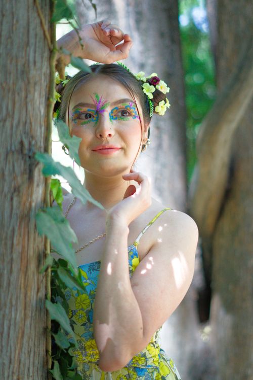 Free A young woman with colorful face paint and floral adornments poses in a forest. Stock Photo