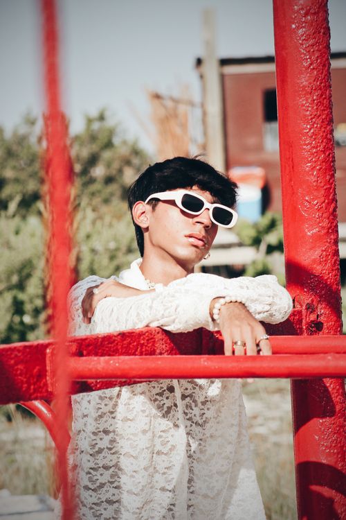 Free A young man in stylish sunglasses and lace shirt poses outdoors in bright sunlight. Stock Photo