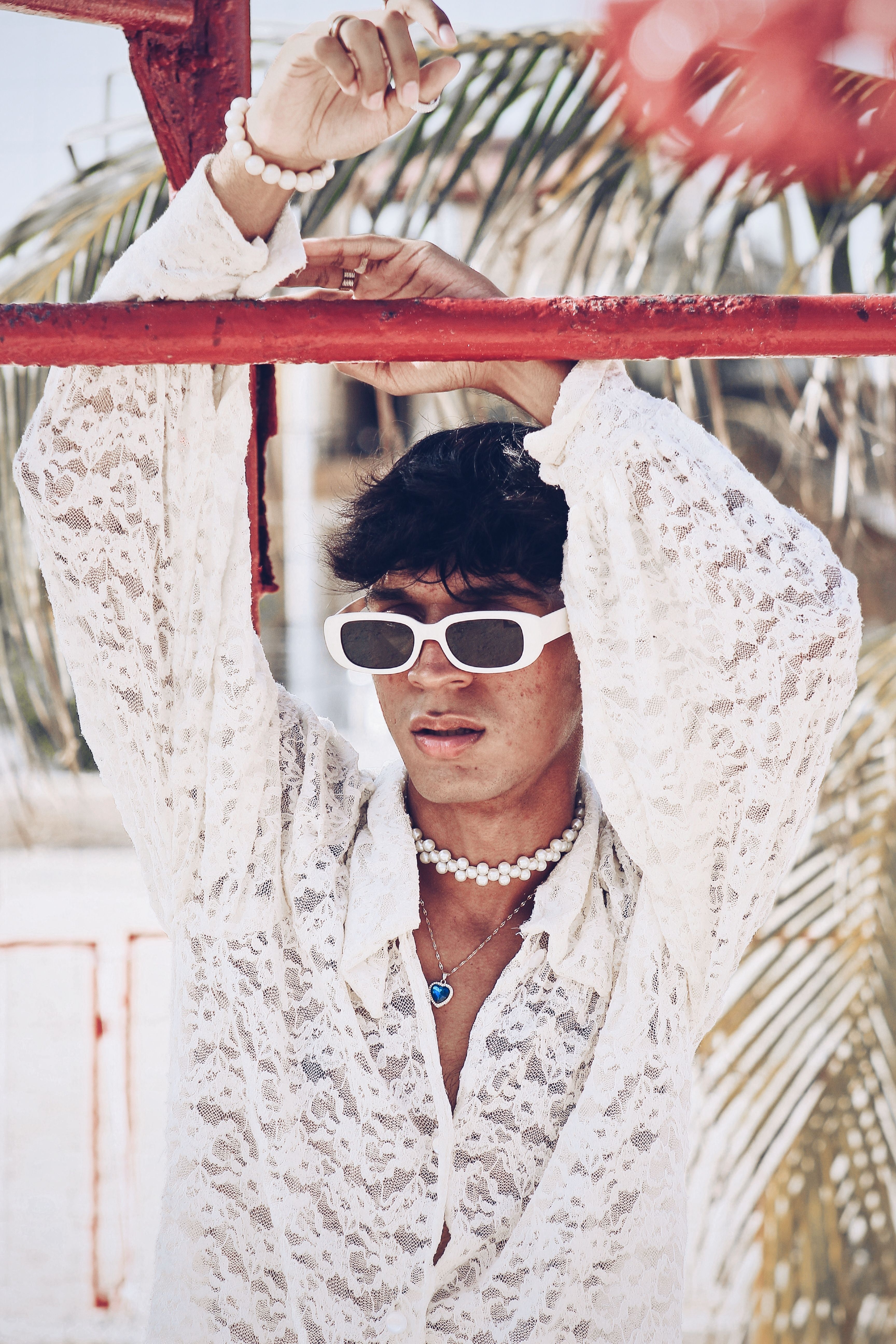 Stylish person wearing sunglasses and pearls in a white lace shirt posing outdoors.