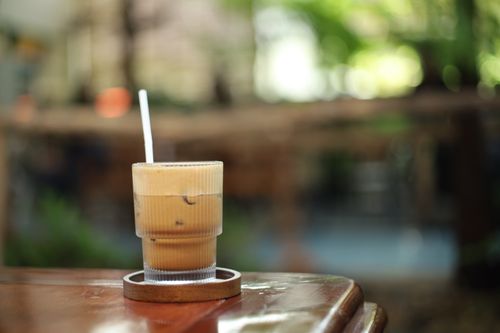 Free Iced coffee in a glass with a straw on a wooden table, outdoors. Stock Photo
