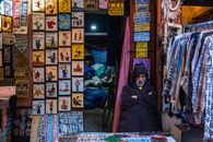 A vendor in Marrakech souk, surrounded by vibrant signs and garments, embodies local culture.