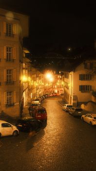 A cozy European street at night with warm lights and cobblestone pavement.