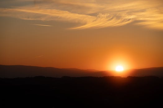 Explore the serene beauty of a sunset casting warm orange hues over tranquil hills, creating a perfect peaceful atmosphere.