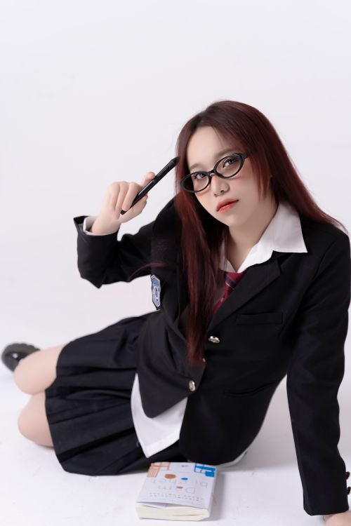 Free Portrait of a young woman in a school uniform, posing with glasses and a pen on a white background. Stock Photo