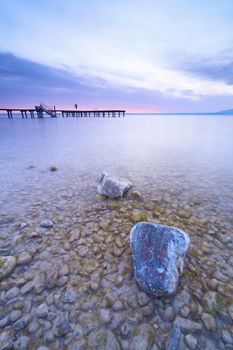 Calm lake scene in Bavaria, Germany with a pier at sunrise, featuring clear waters and rocks.