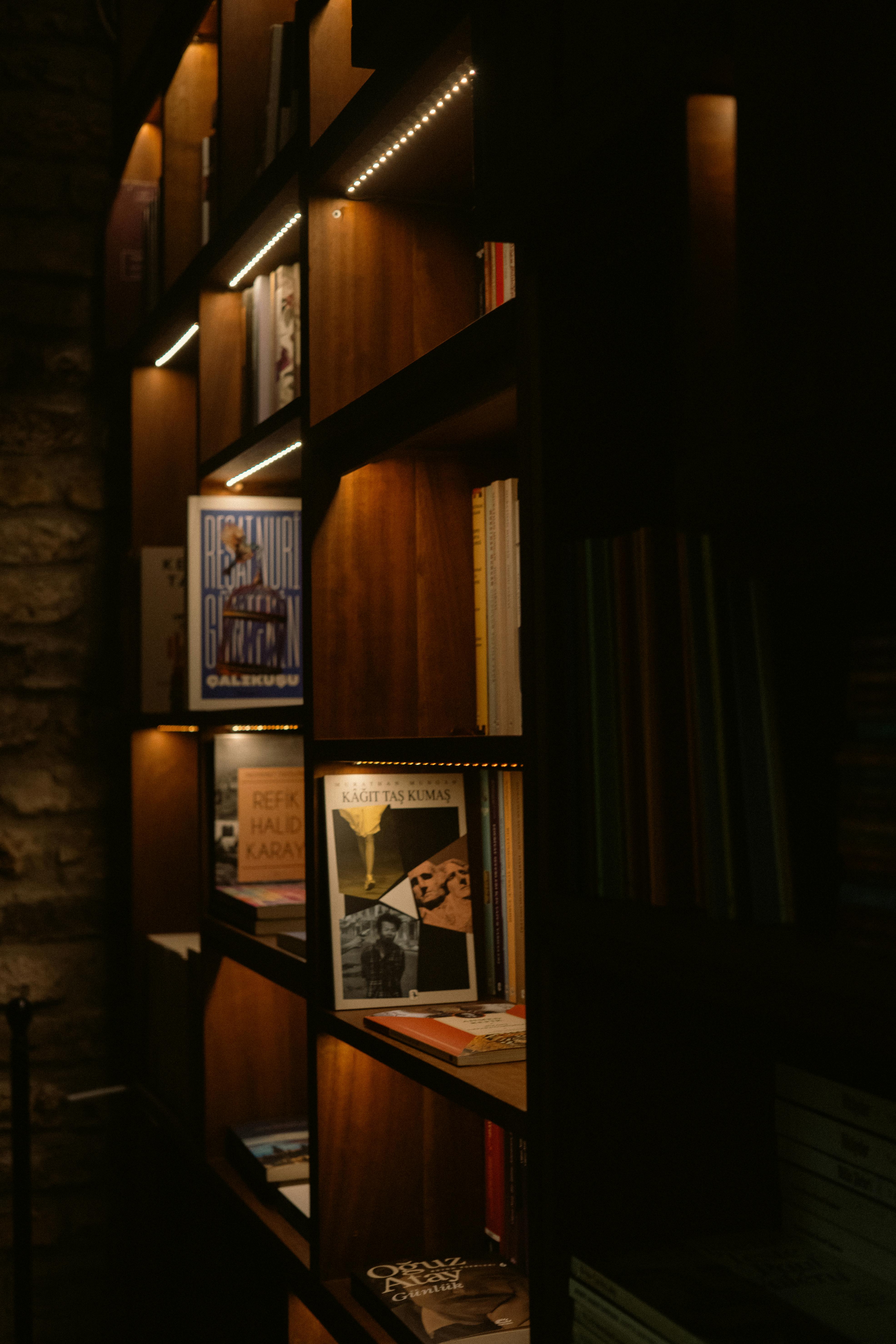 Gratis Una libreria illuminata in modo caldo e piena di libri di vario tipo crea un'accogliente atmosfera da biblioteca. Foto a disposizione