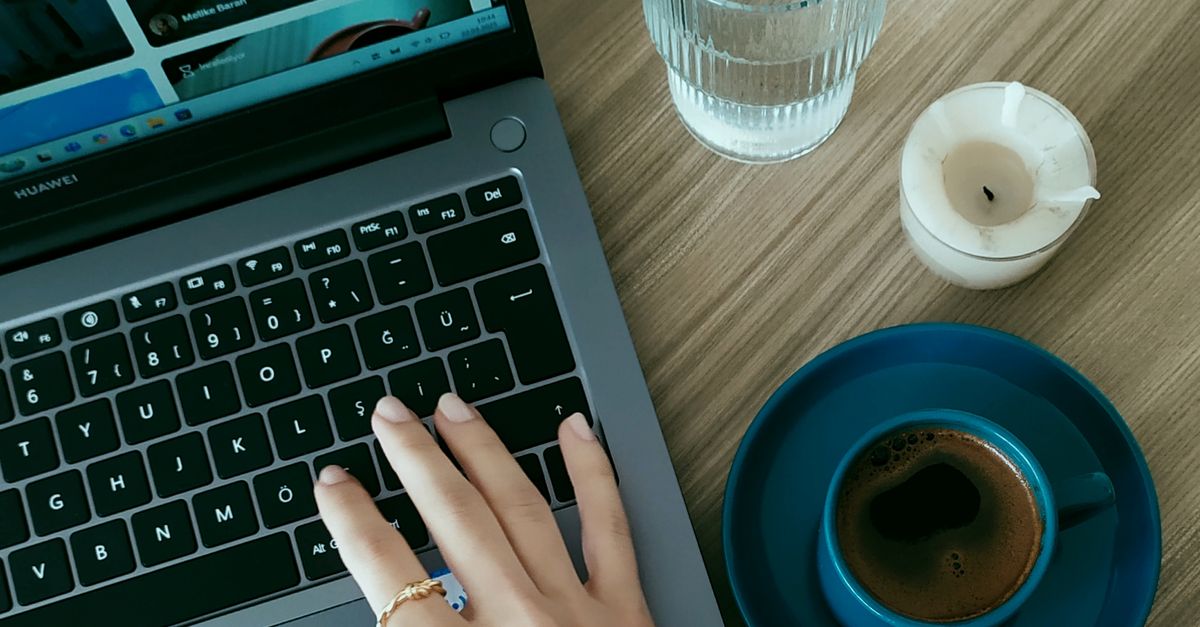 Vista aérea de una mano en una computadora portátil junto a café y agua, configuración de escritorio acogedora. Vista aérea de una mano en una computadora portátil junto a café y agua, configuración de escritorio acogedora.