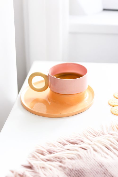 Free A pink coffee cup on an orange plate creating a modern, minimalist vibe. Stock Photo