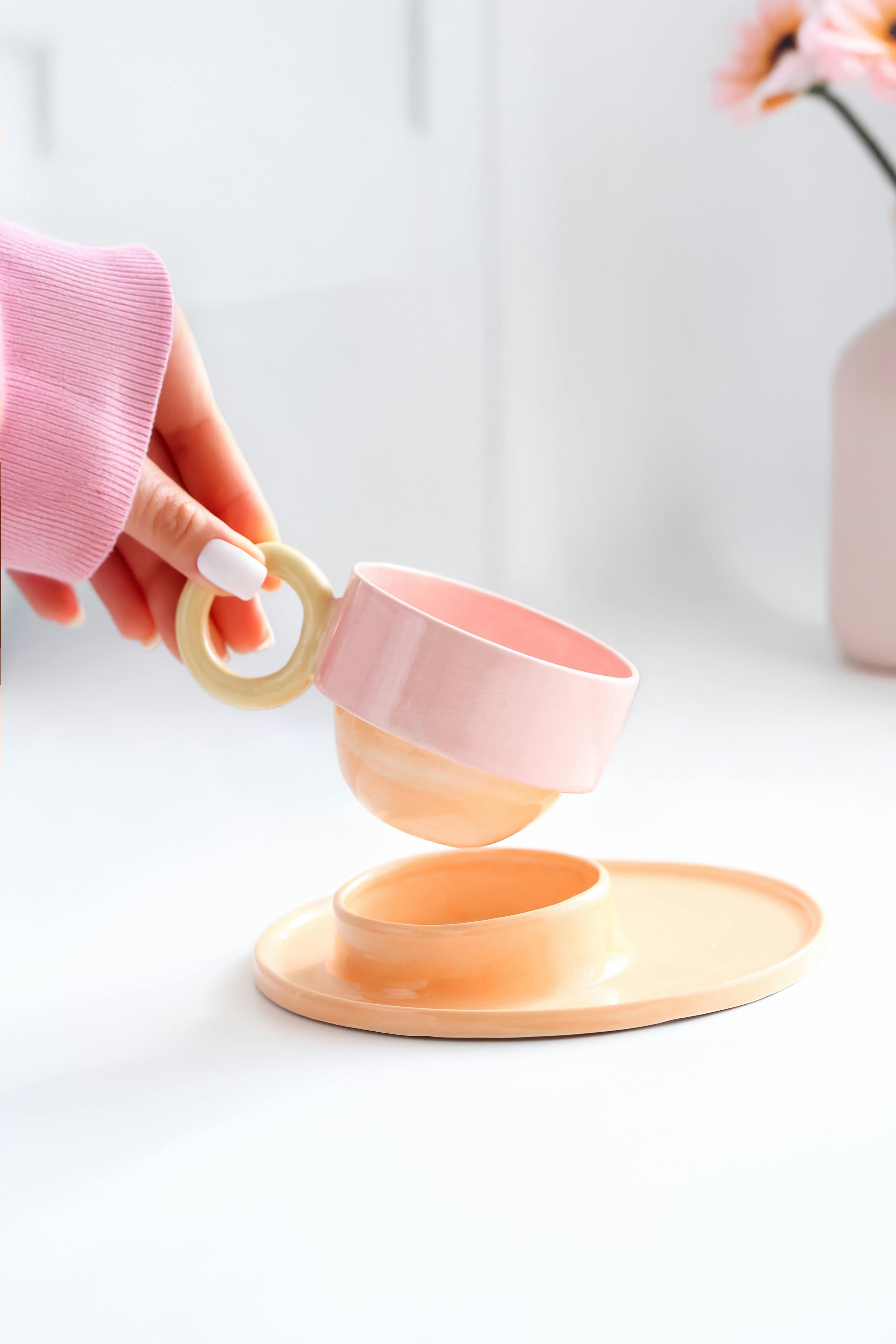 Stylish pink teacup and saucer set held by a woman in a cozy setting.