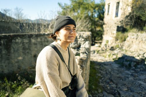 Free A woman smiles outdoors wearing winter clothes, against a rustic backdrop. Stock Photo
