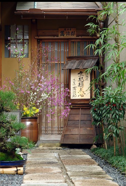 Free A serene traditional Japanese entrance adorned with blooming flowers and bamboo plants. Stock Photo