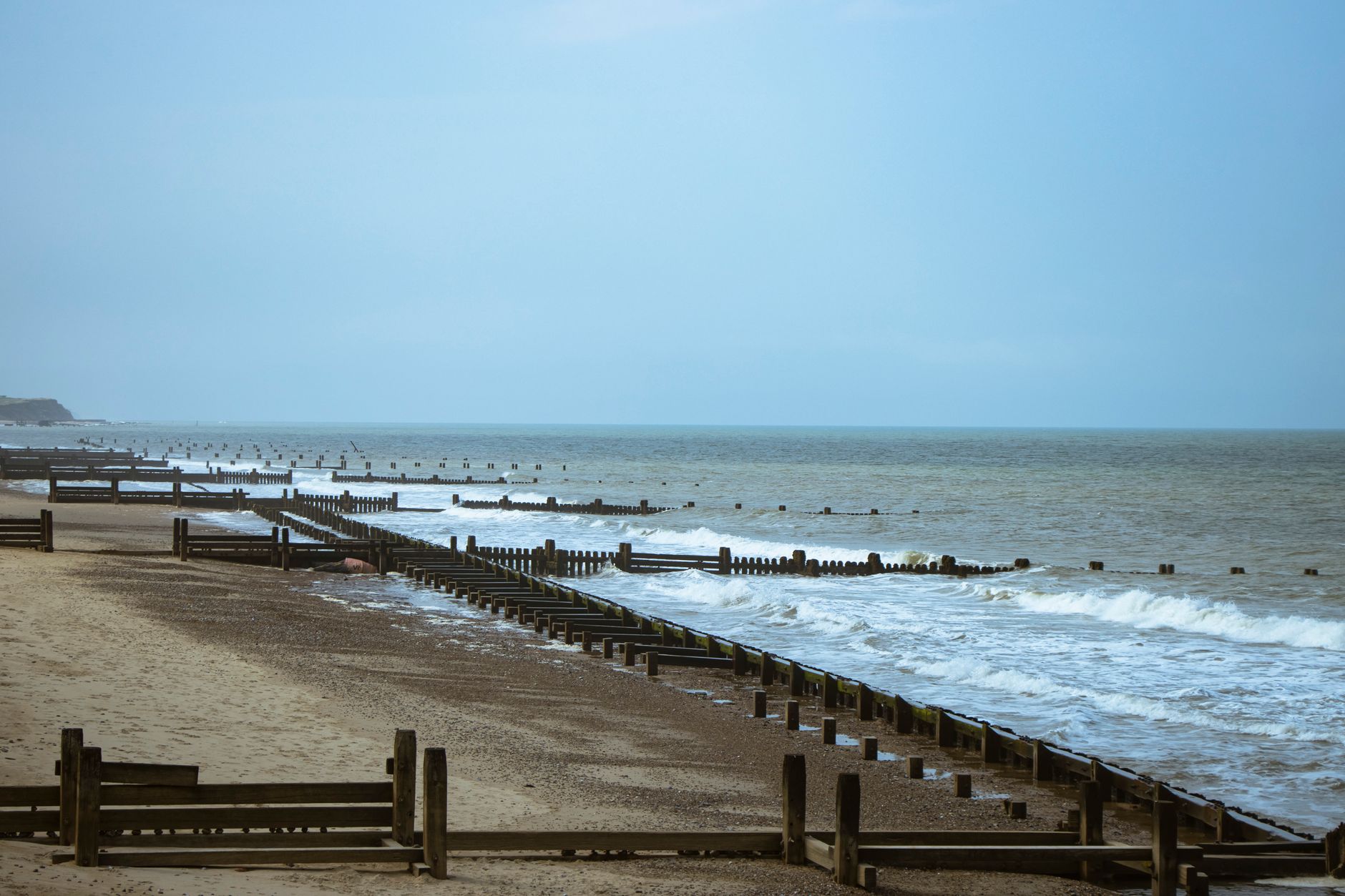 A serene coastal scene featuring wooden groynes by the sea in England on a moody day.