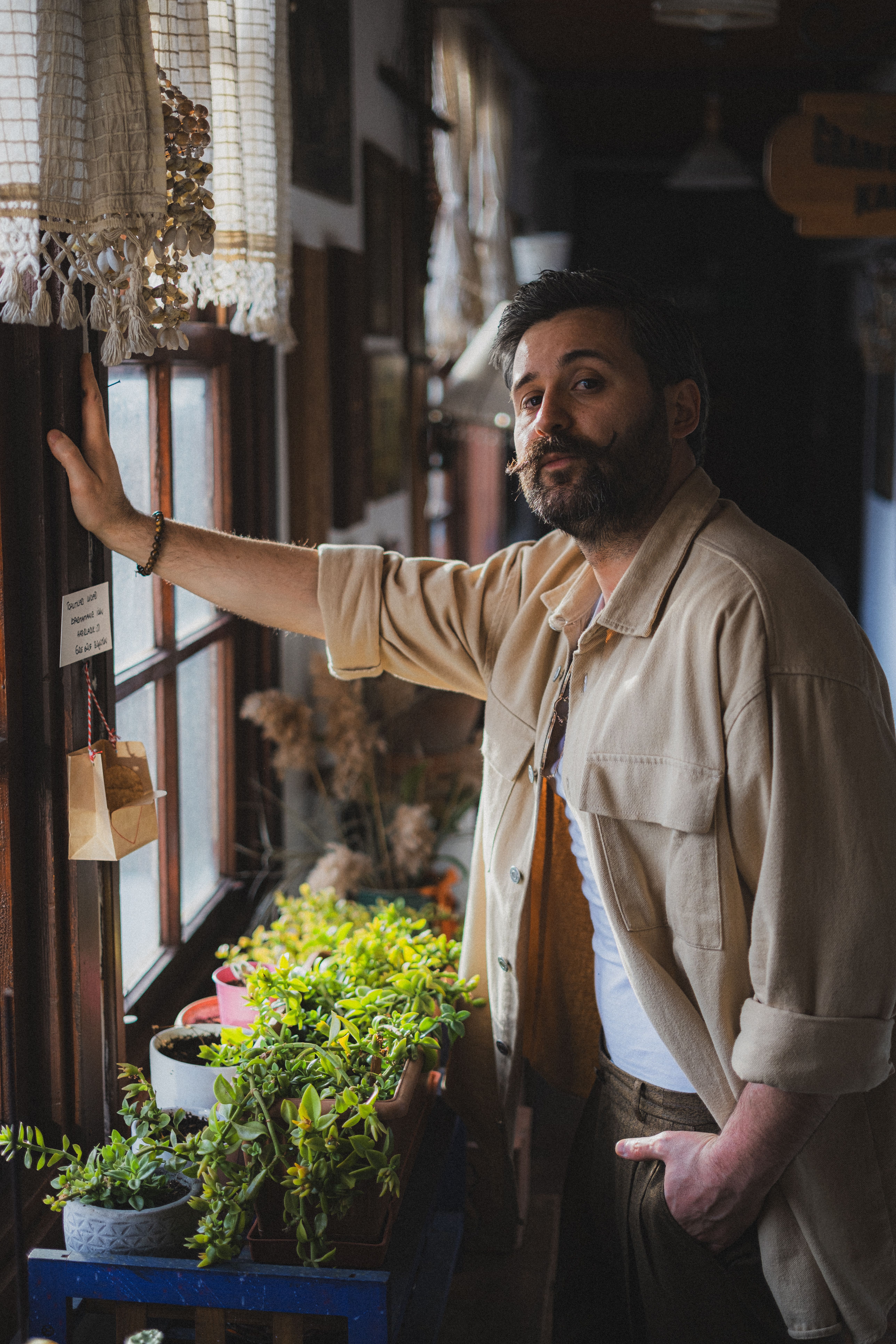 A man stands by a sunlit window with potted plants, enjoying a serene indoor moment.