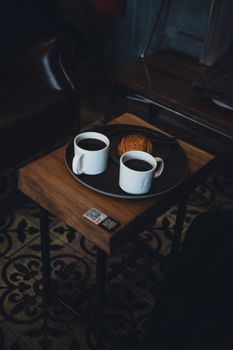 Two cups of coffee with a pastry on a table, perfect for a cozy breakfast date.