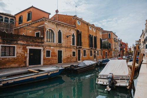 Free Beautiful view of traditional Venice canal with gondolas and historic brick buildings under a blue sky. Stock Photo