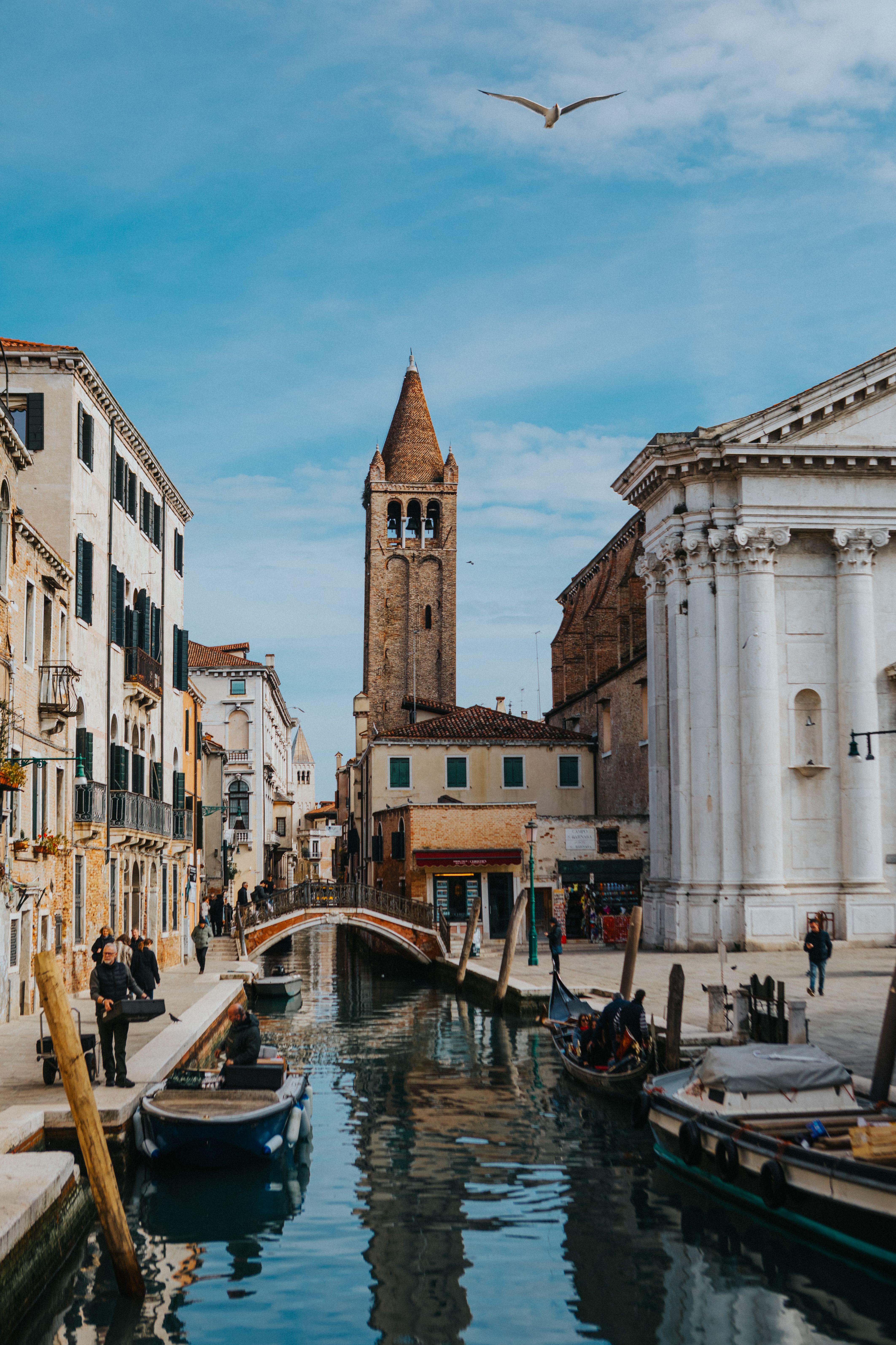 Historic canal scene in Venice featuring a charming bridge and iconic architecture under a bright blue sky.