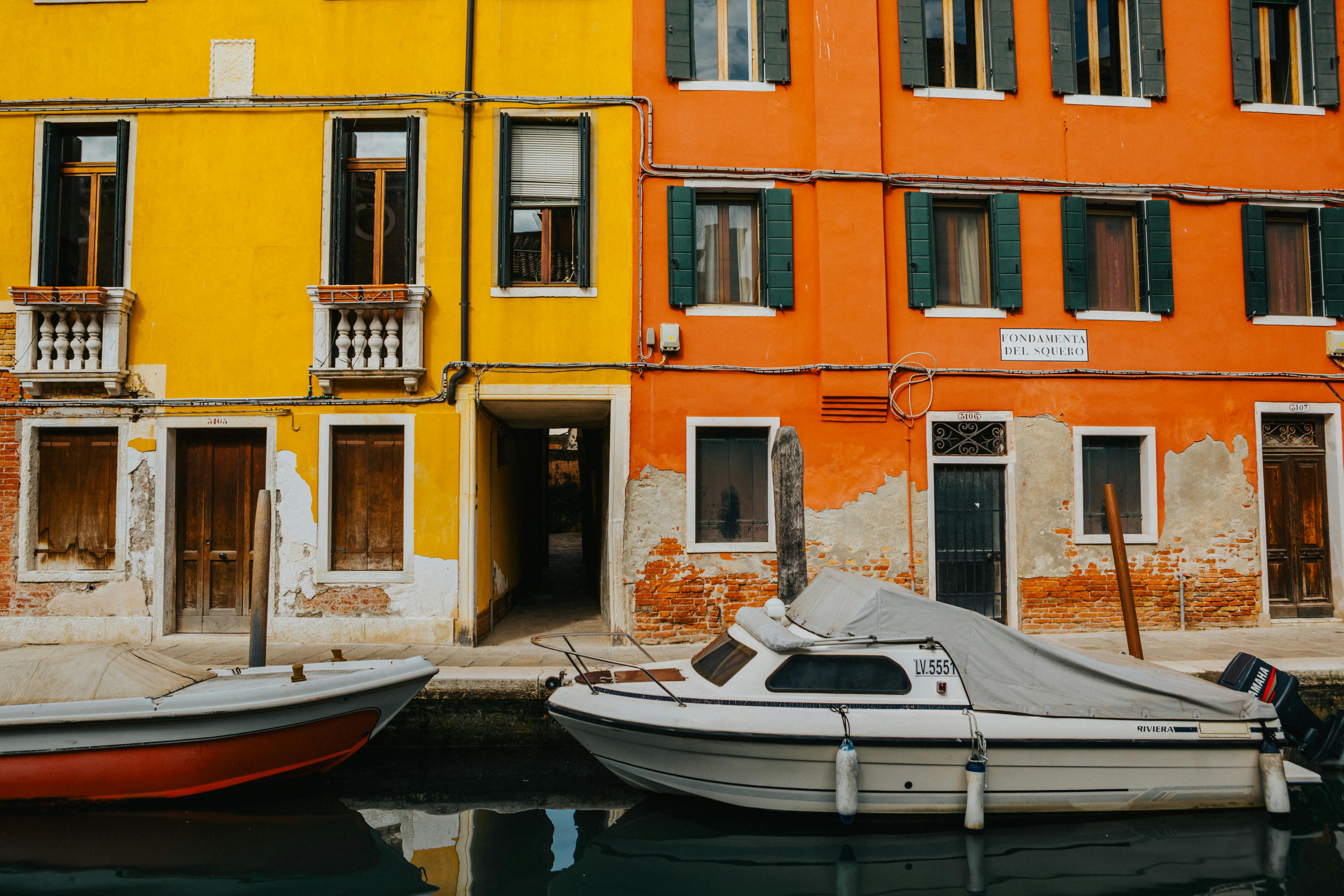 Colorful Venetian buildings alongside a canal with boats moored in front under a clear sky.