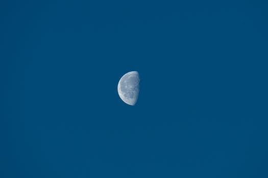 A clear view of the half moon set against a vibrant blue daytime sky.