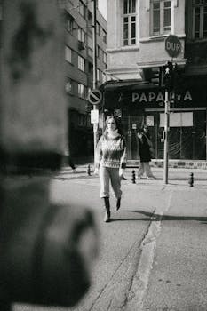 Black and white photo capturing a person walking in an urban street setting.