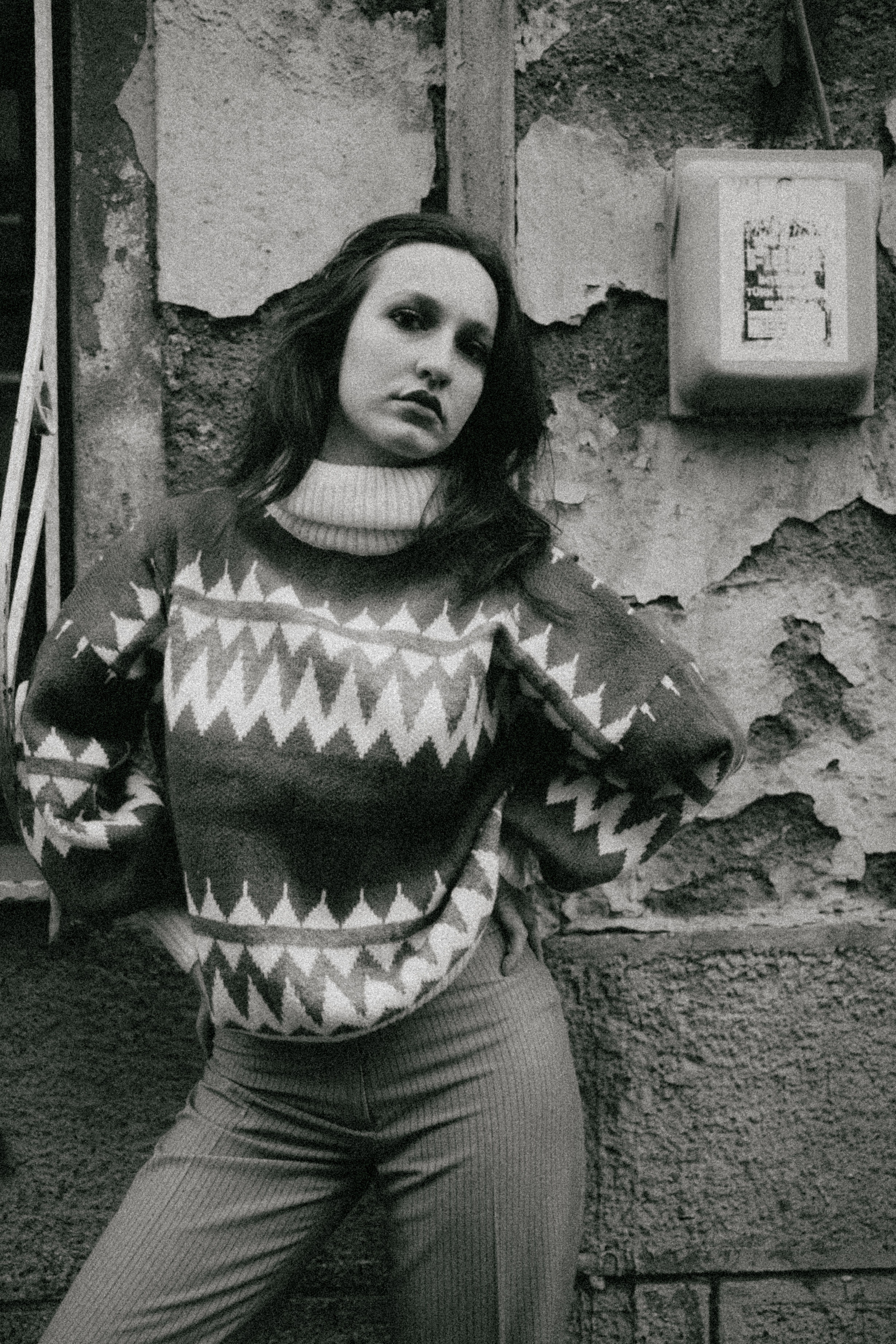 Fotomural Un retrato clásico en blanco y negro de una mujer con un suéter de patrón, posando frente a una pared texturizada.