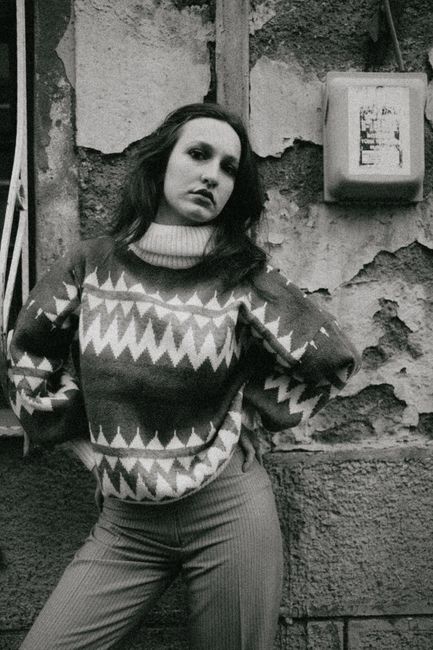 Fotomural Un retrato clásico en blanco y negro de una mujer con un suéter de patrón, posando frente a una pared texturizada.