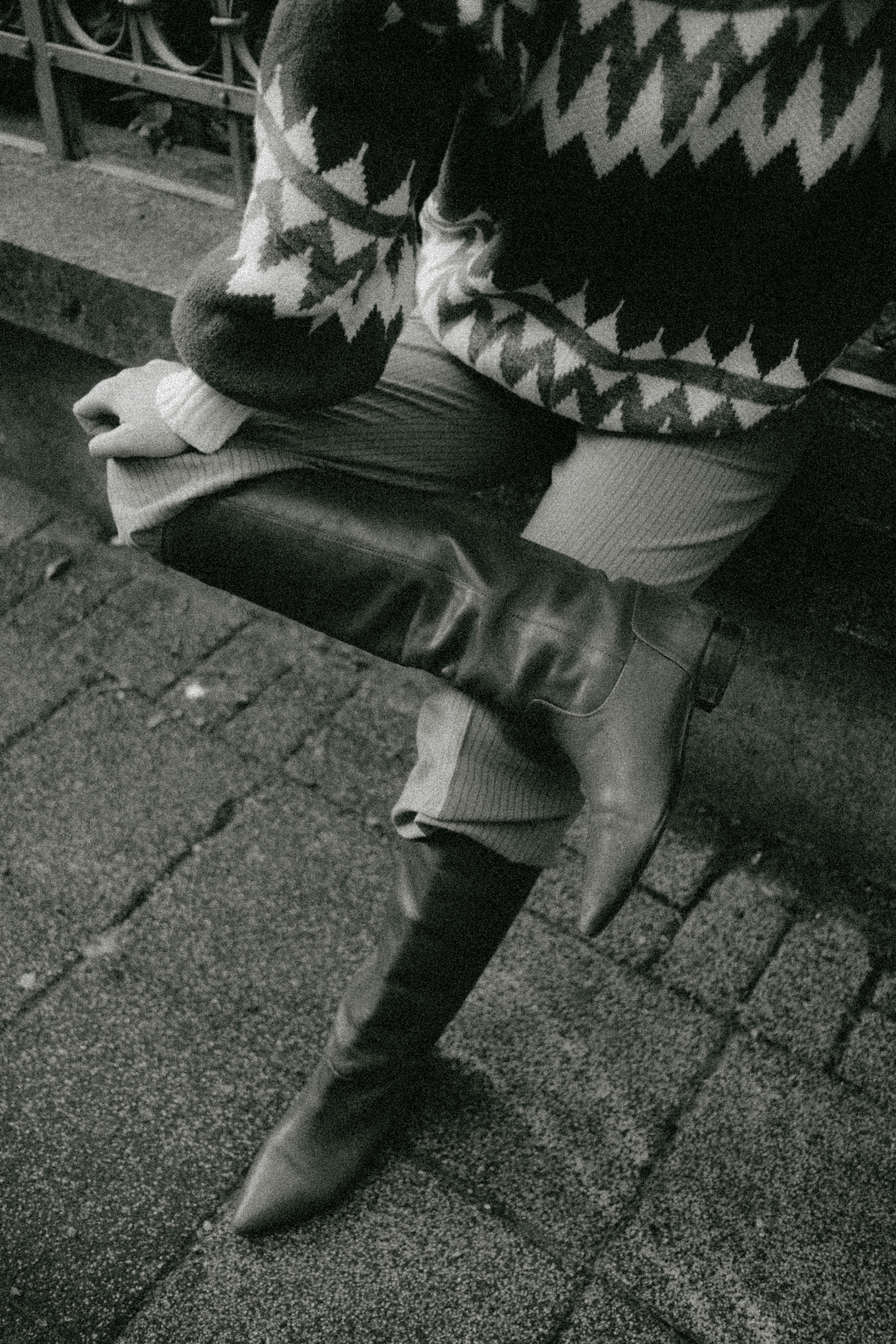 Monochrome image of a person wearing a knitted sweater and knee-high boots on a city street.