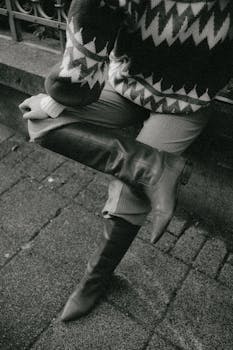 Monochrome image of a person wearing a knitted sweater and knee-high boots on a city street.