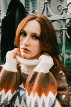 Warm autumn portrait of a woman with red hair in a patterned knit sweater outdoors.