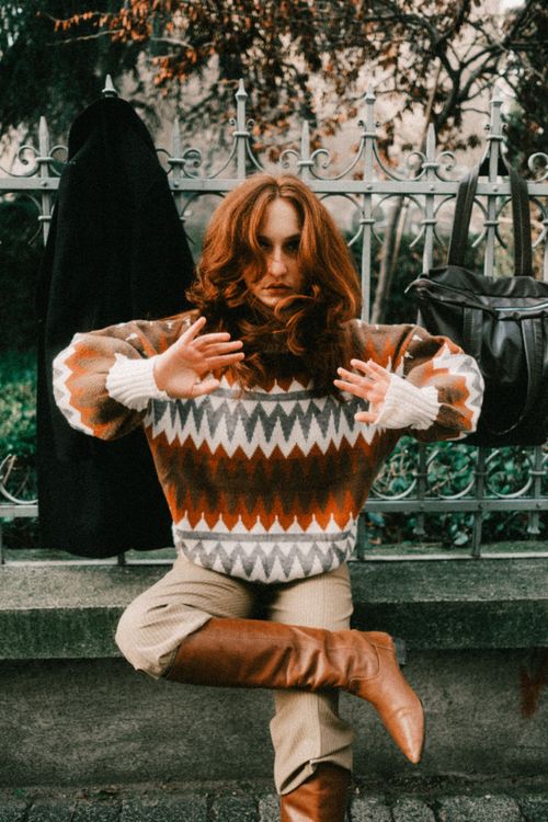 Free Trendy woman with red hair poses in chic sweater and boots outdoors. Stock Photo