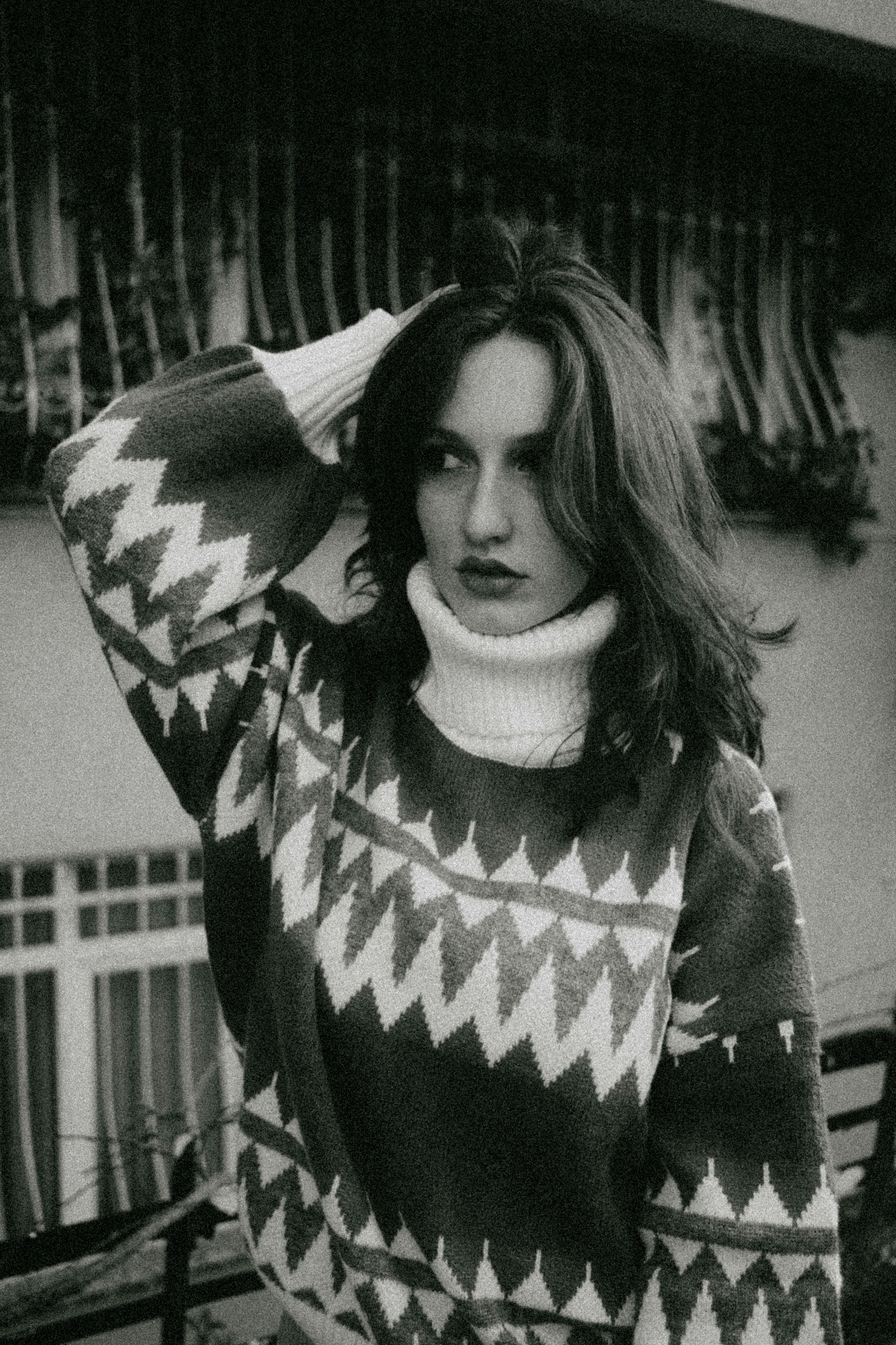 Fashionable woman in a patterned sweater posing outside urban setting. Black and white.