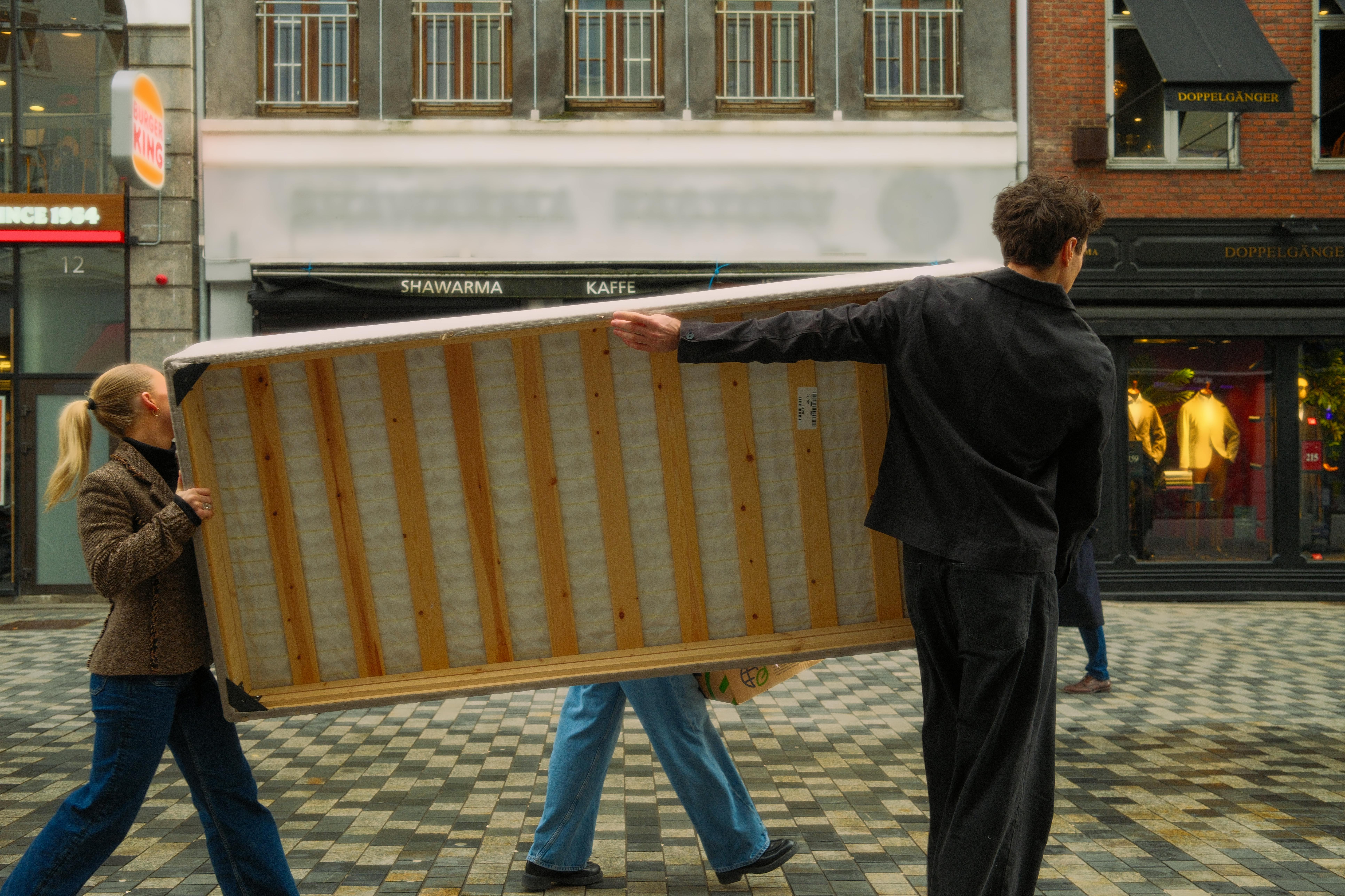 Several people carrying a mattress across a busy street in an urban environment.
