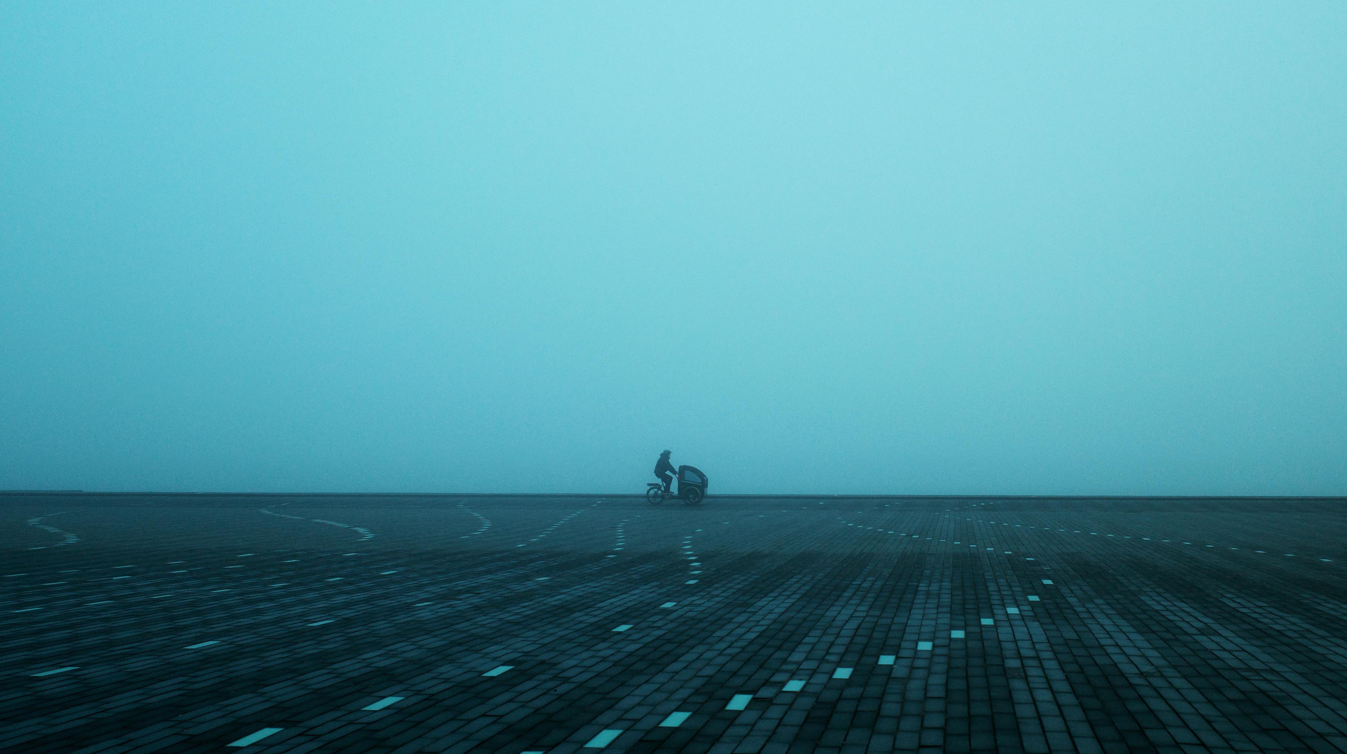 A misty scene in Aalborg, Denmark, featuring a lone cyclist on a paved square, evoking solitude.
