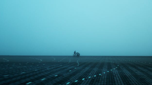 A misty scene in Aalborg, Denmark, featuring a lone cyclist on a paved square, evoking solitude.