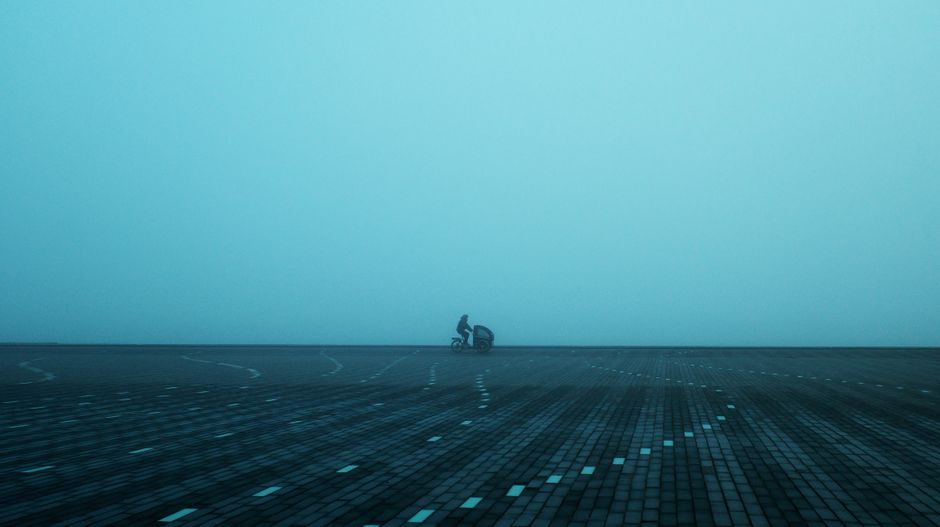 A misty scene in Aalborg, Denmark, featuring a lone cyclist on a paved square, evoking solitude.